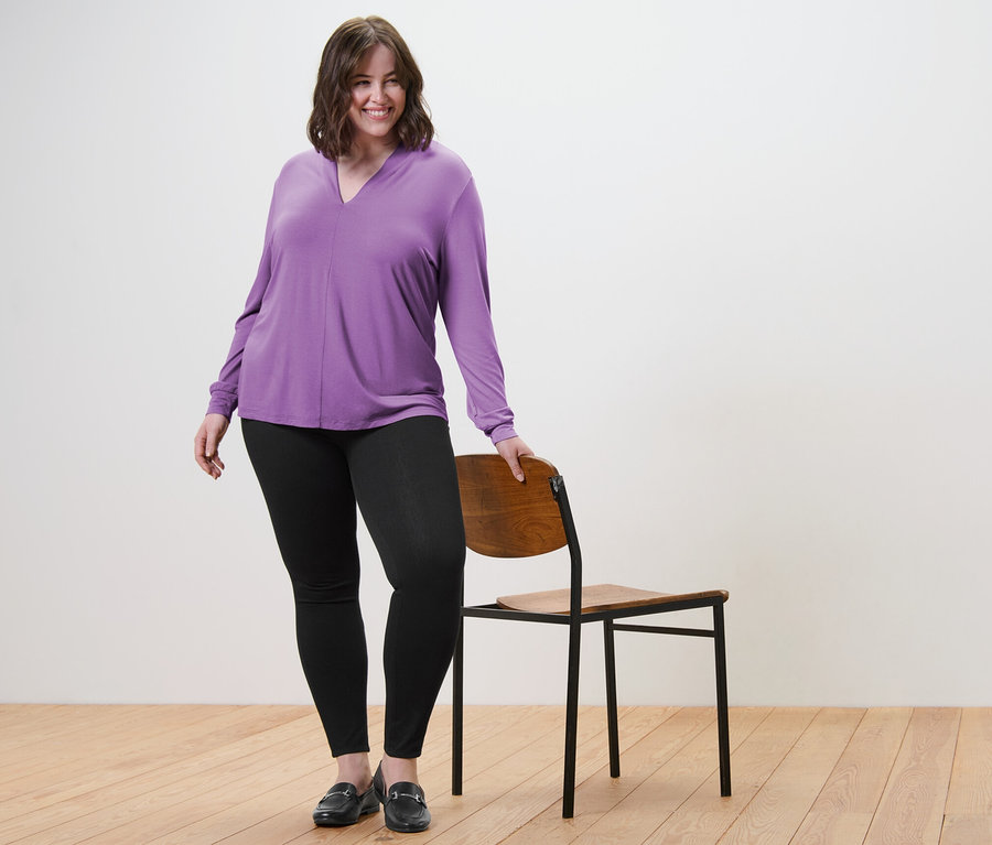 Žena pózuje v halence s výstřihem do V a v džegínách.