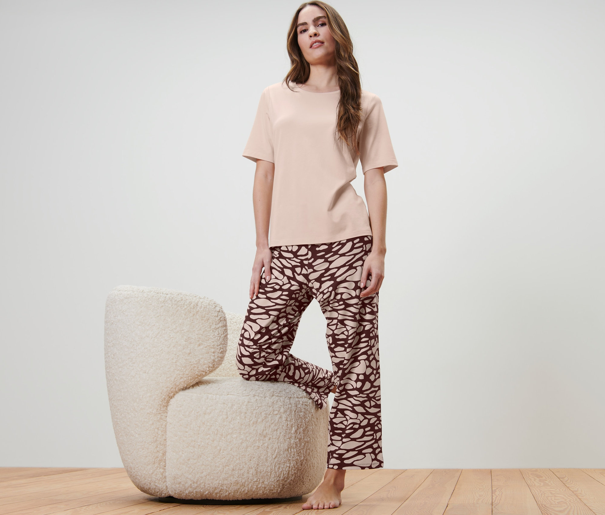 Žena pózuje s jednou nohou na chlupatém křesle a má na sobě pyžamo.