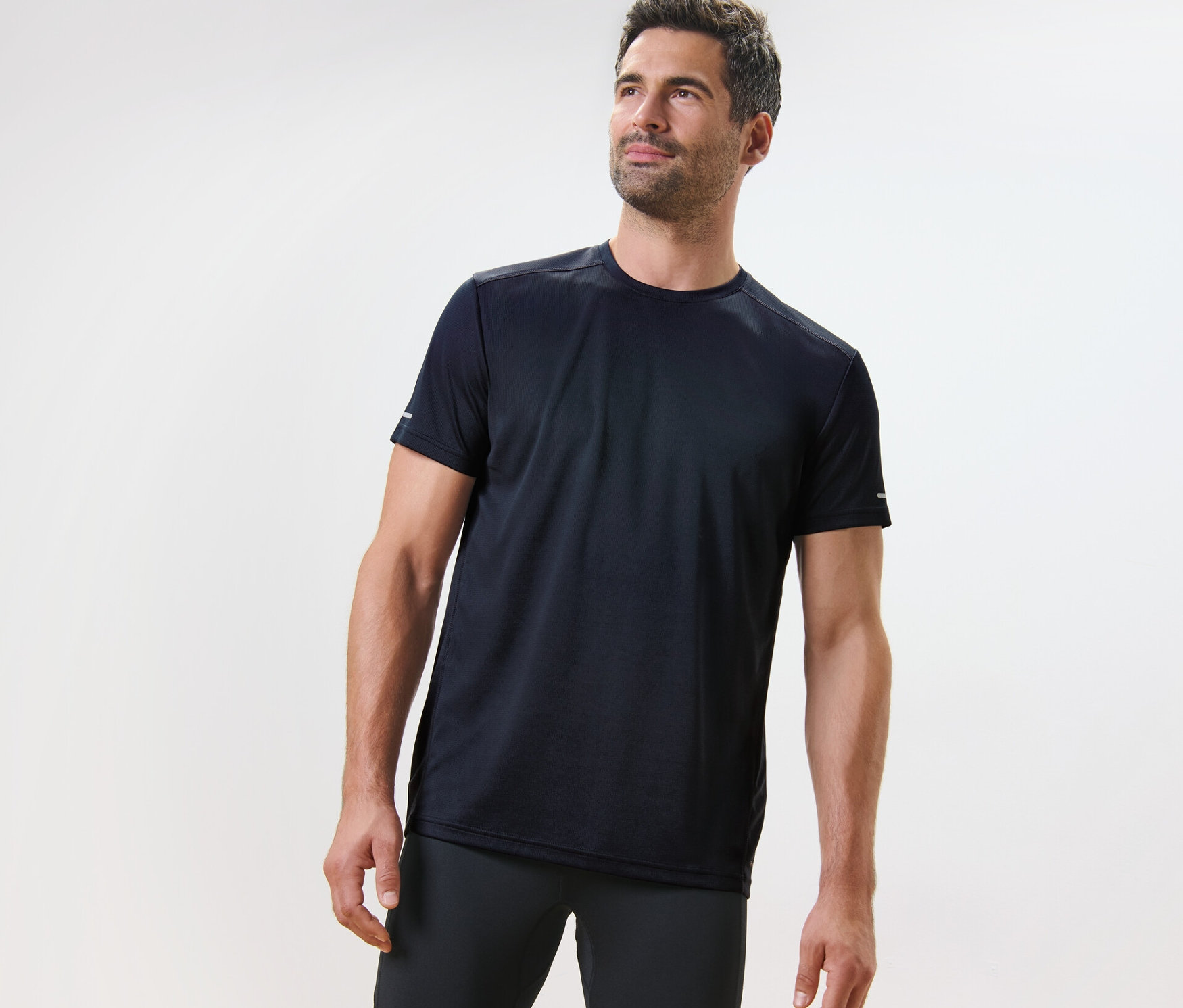 Muž v námořnicky modrém funkčním tričku stojí na světlém pozadí.