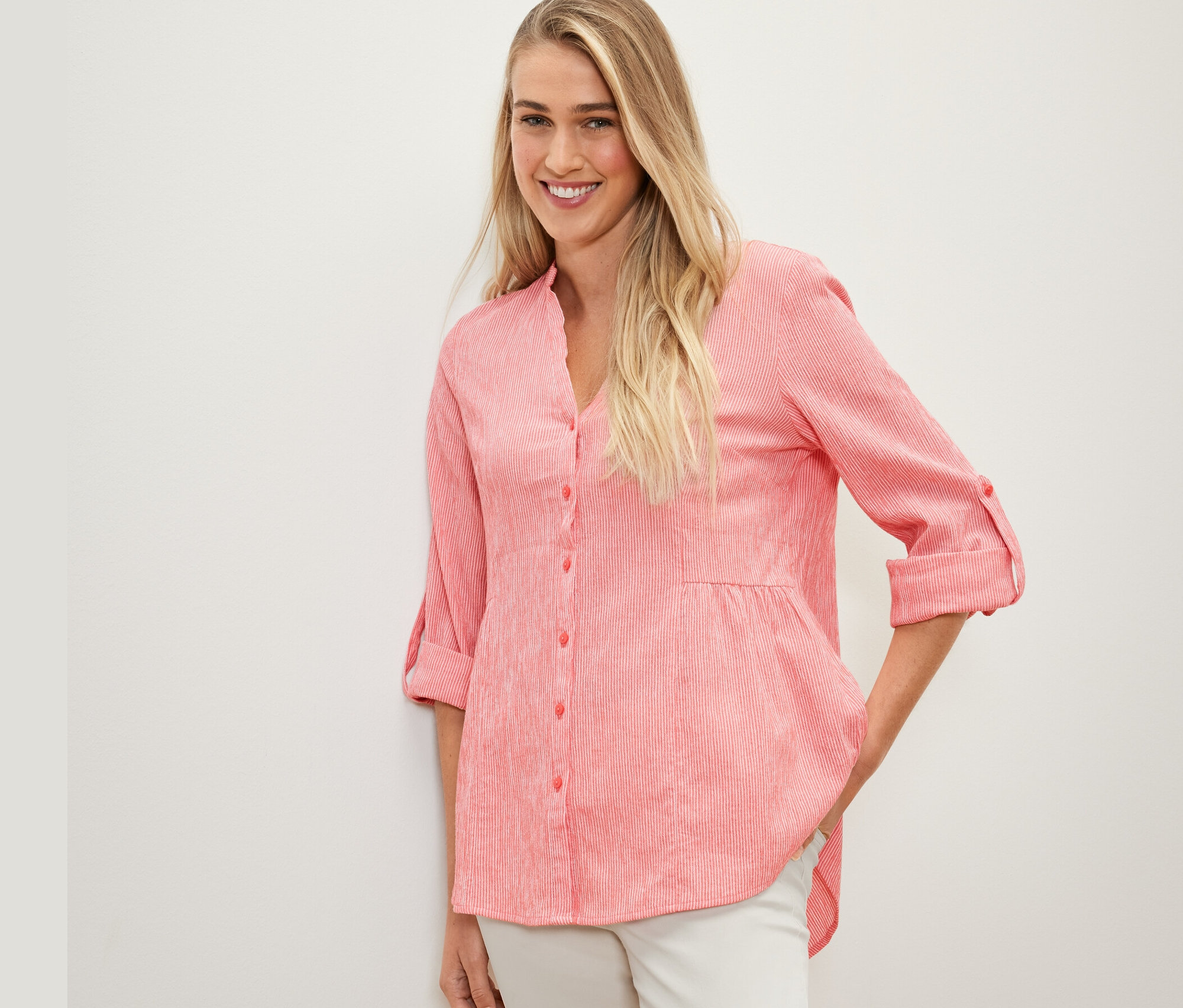 Žena pózuje v korálové tunice s proužky.