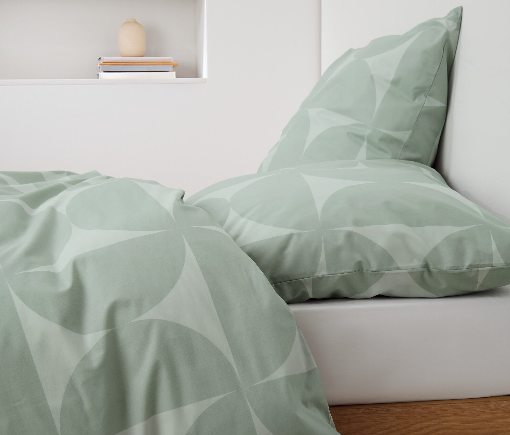 Zelené povlečení renforcé s geometrickým vzorem na posteli.