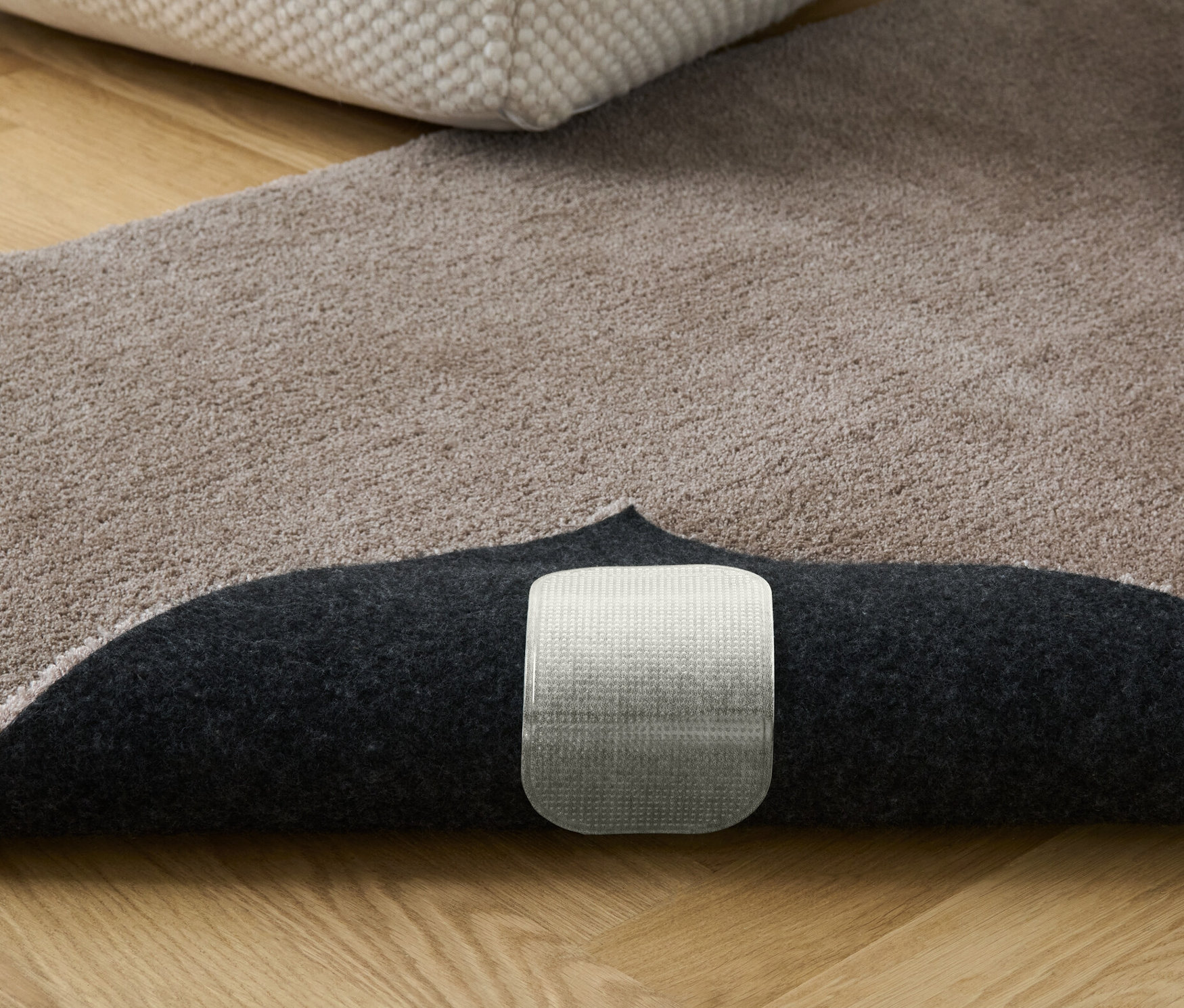 Béžový koberec s knihami a podnožkou. Viditelné jsou protiskluzové podložky pod koberec, 4 ks.