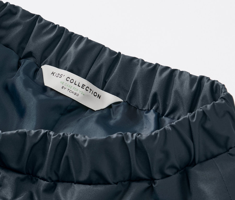 Detail dětských kalhot do deště tmavě modré barvy s elastickým pasem a štítkem Kids' Collection.