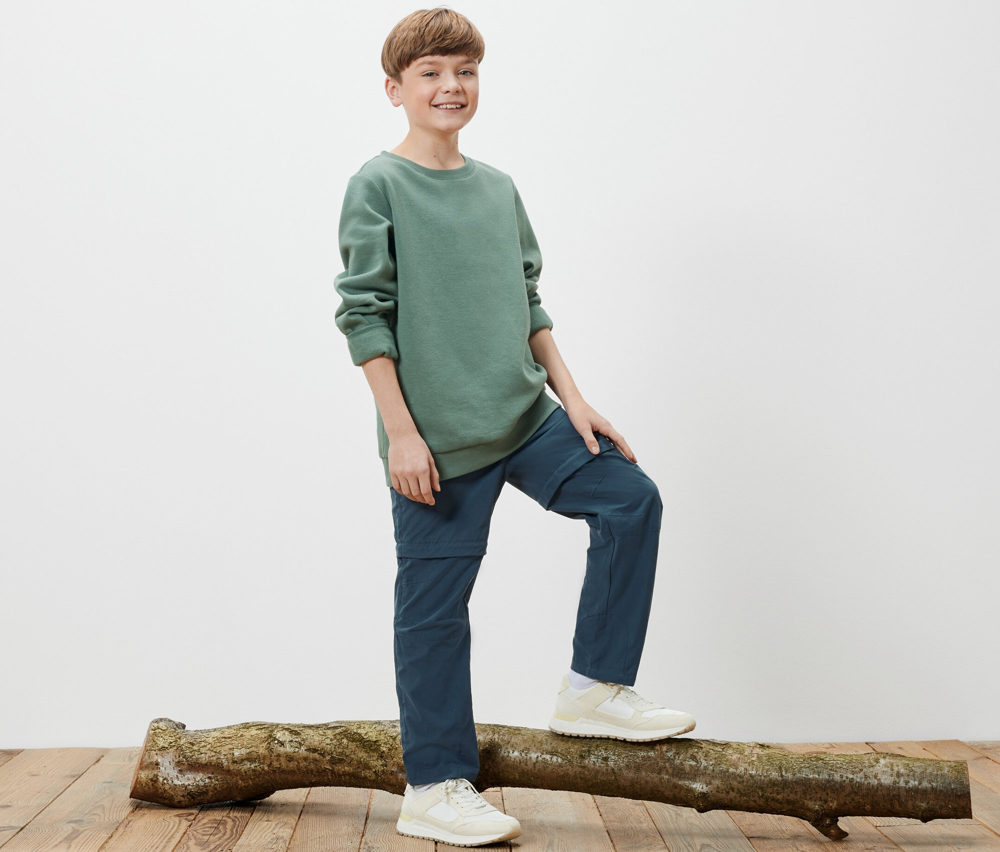 Chlapec stojí na kmeni stromu a má na sobě dětské funkční kalhoty.