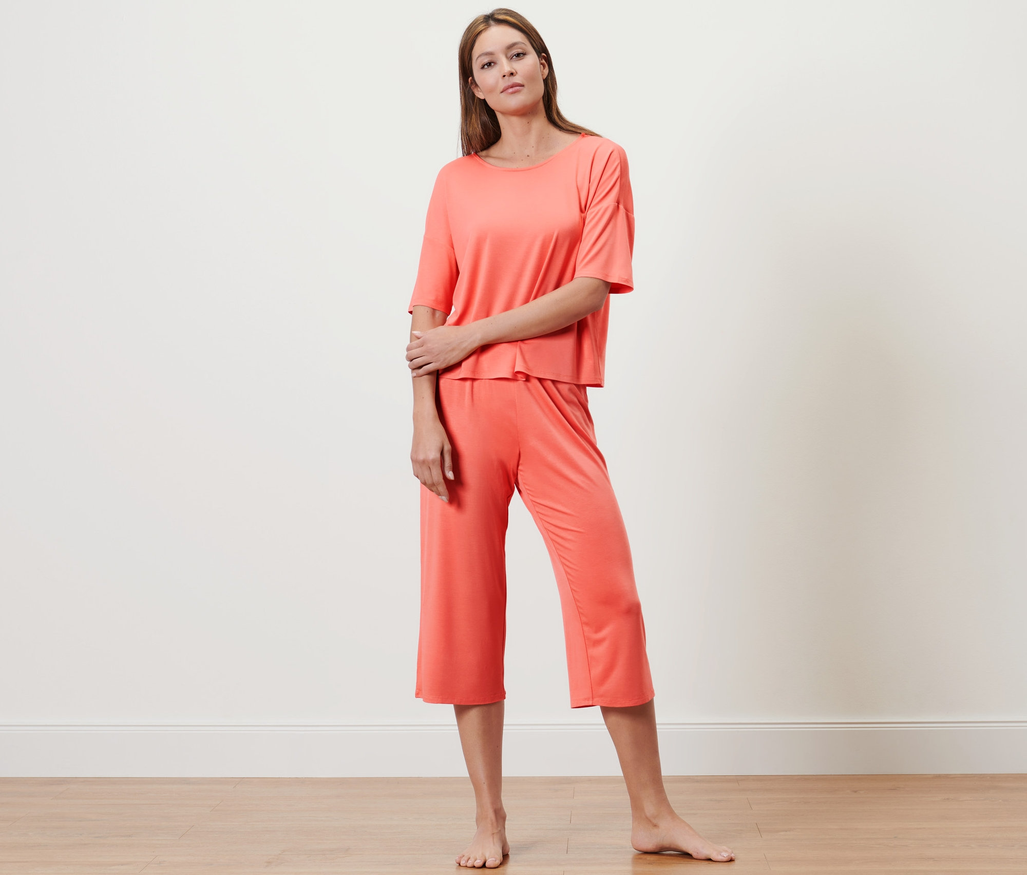 Žena pózuje v lososovém pyžamu ve 3/4 délce.