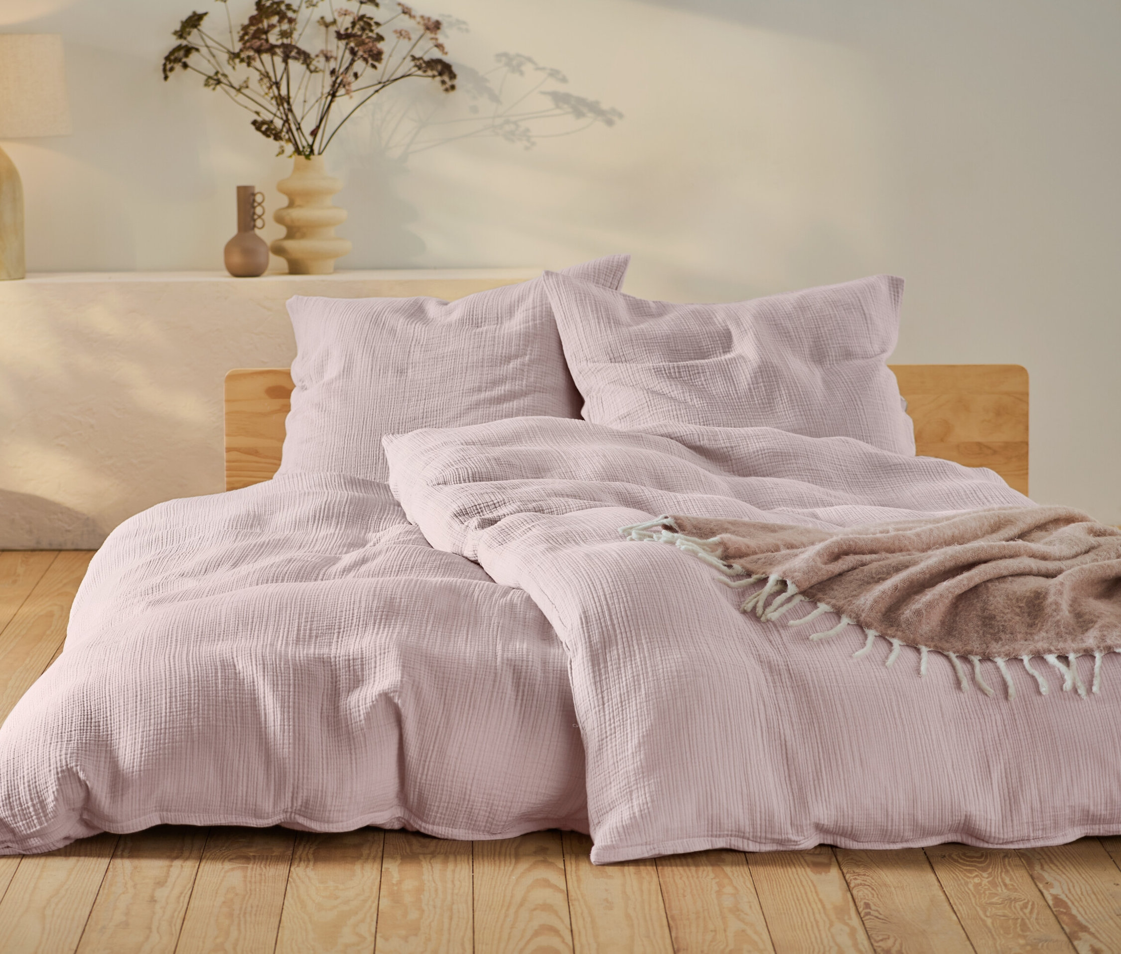 Růžové mušelínové povlečení standardní a nadměrné velikosti na posteli s dřevěným rámem.