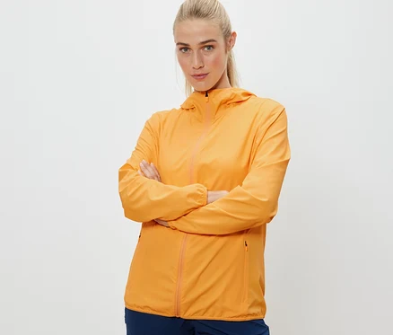 Žena se zkříženýma rukama pózuje v oranžové sbalitelné funkční bundě.