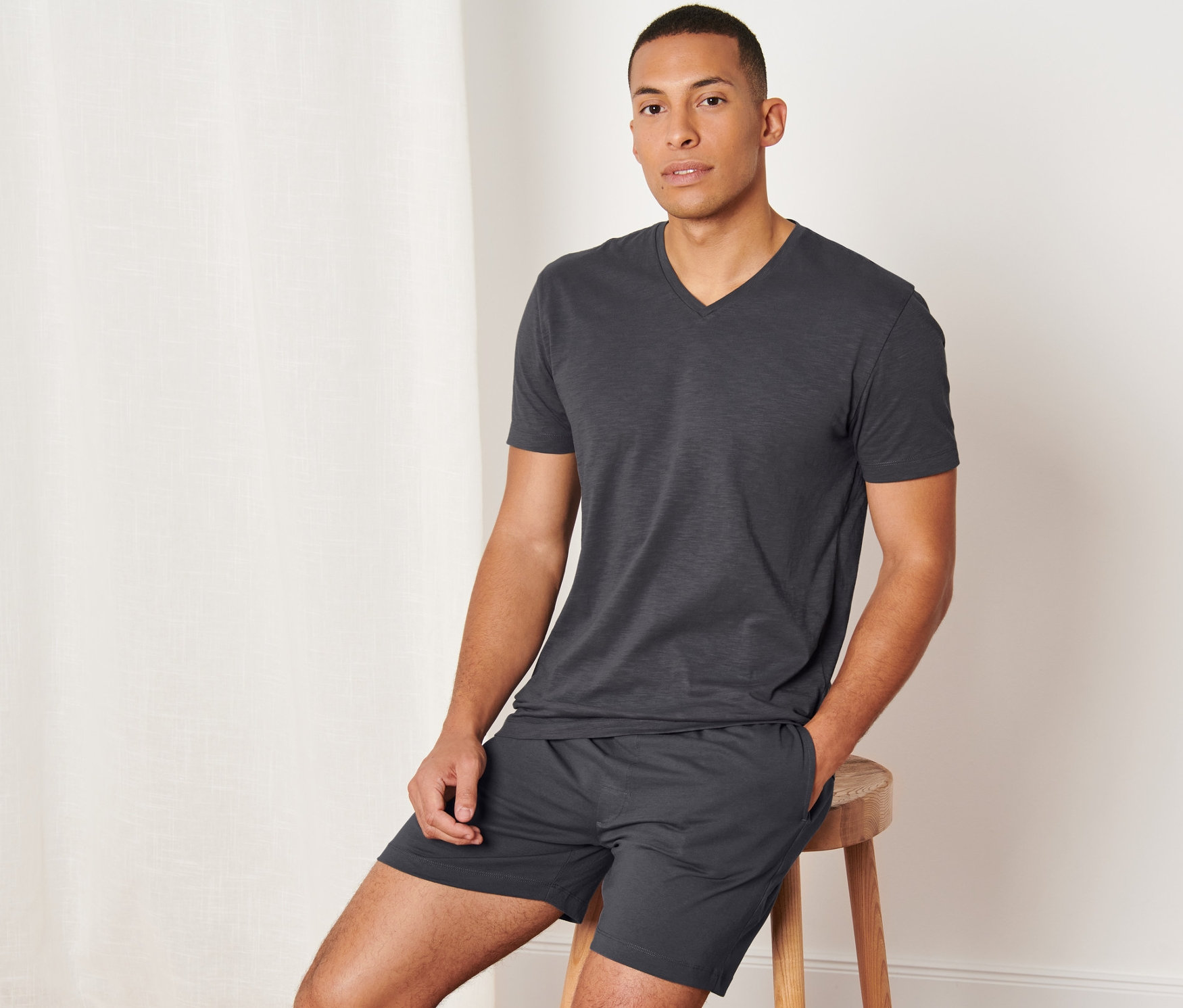 Muž sedí na stoličce a má na sobě krátké antracitové pyžamo.