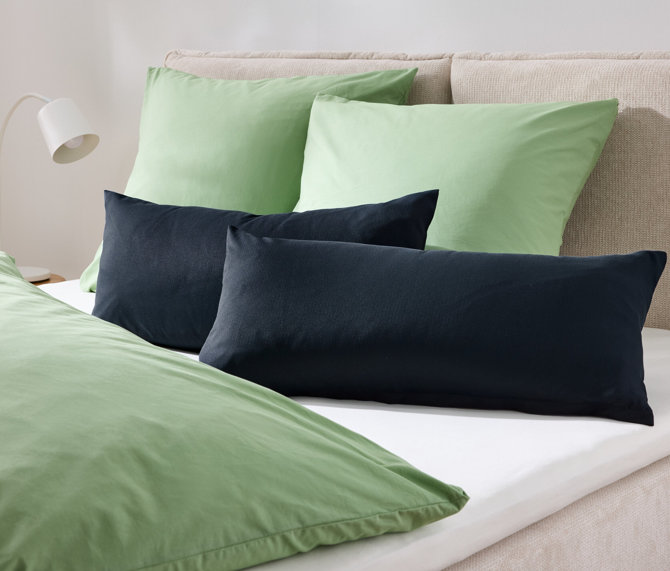 Na posteli jsou dva zelené polštáře a dva tmavě modré polštáře, přikryté zeleným povlečením.