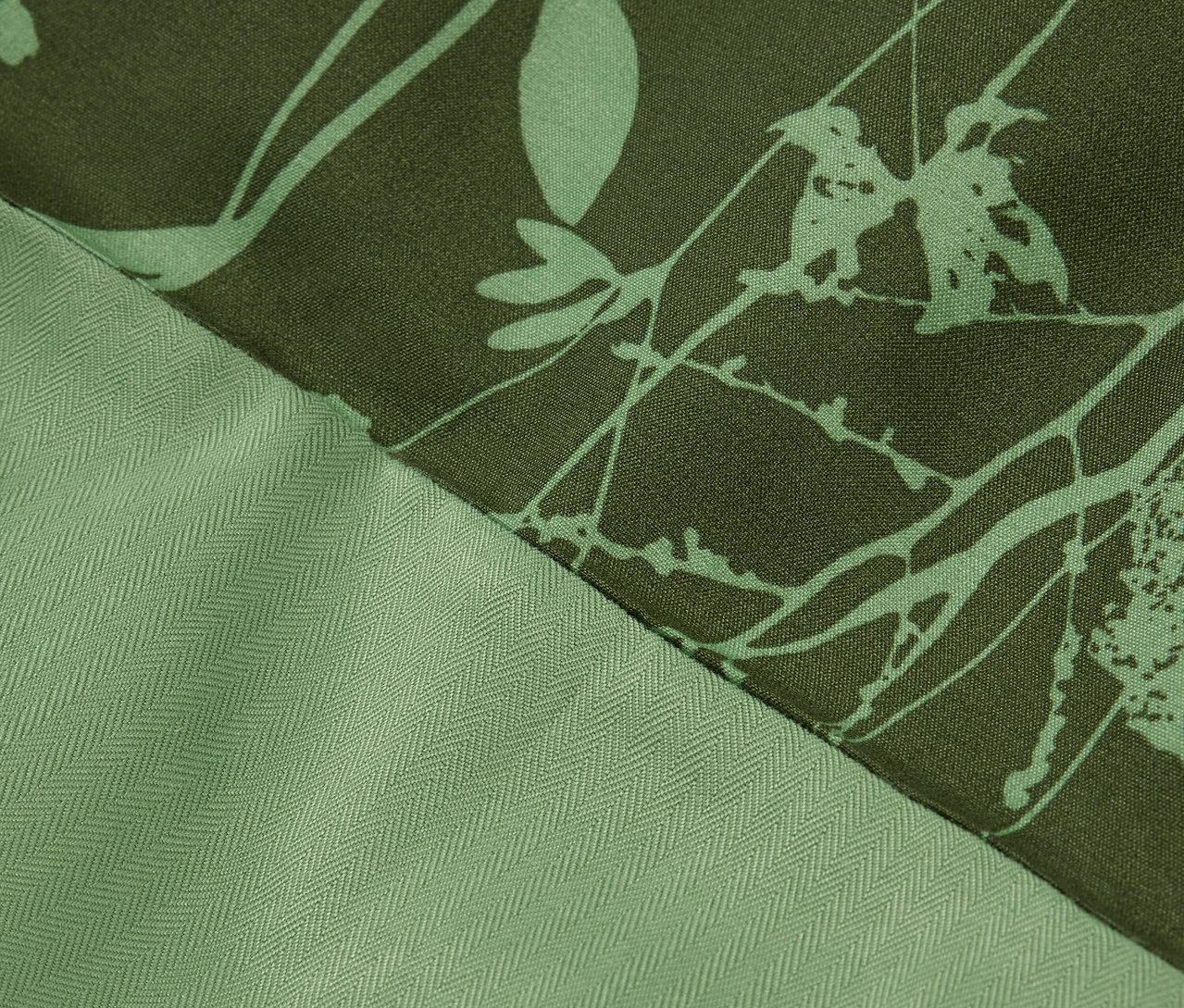 Detail zelené látky s květinovým potiskem a texturou rybí kosti.