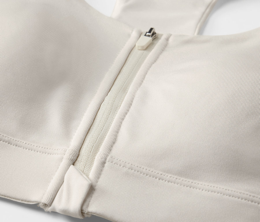 Detailní záběr sportovní podprsenky s předním zipem, barva offwhite.