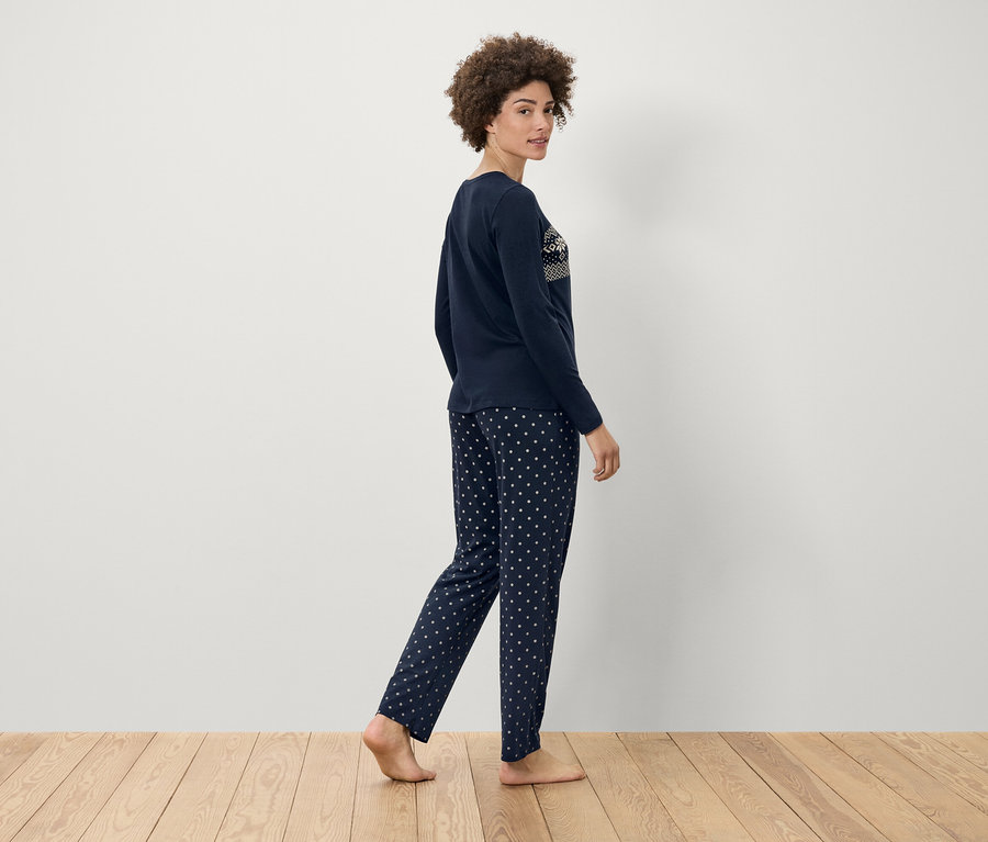 Žena v tmavě modrém pyžamu s bílými puntíky kráčí po dřevěné podlaze.