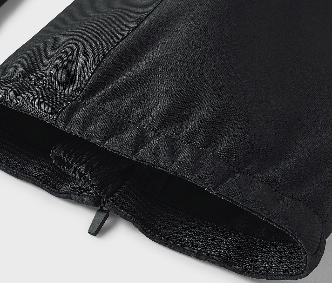 Detail černých kalhot se zipem a elastickým lemem.