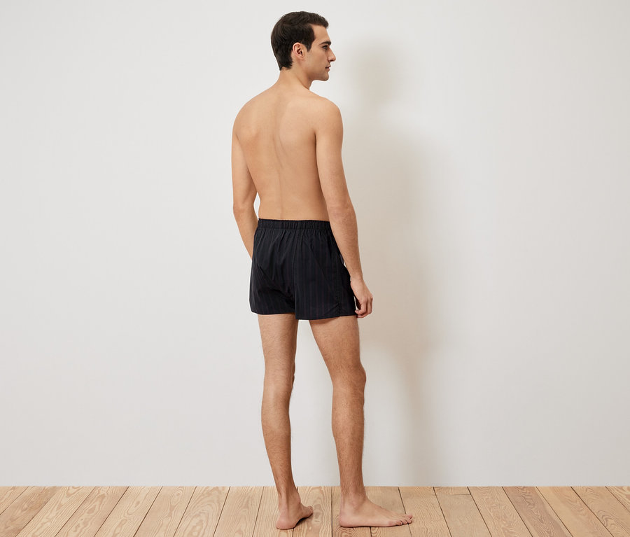 Muž zády, má na sobě černé trenýrky na dřevěné podlaze.