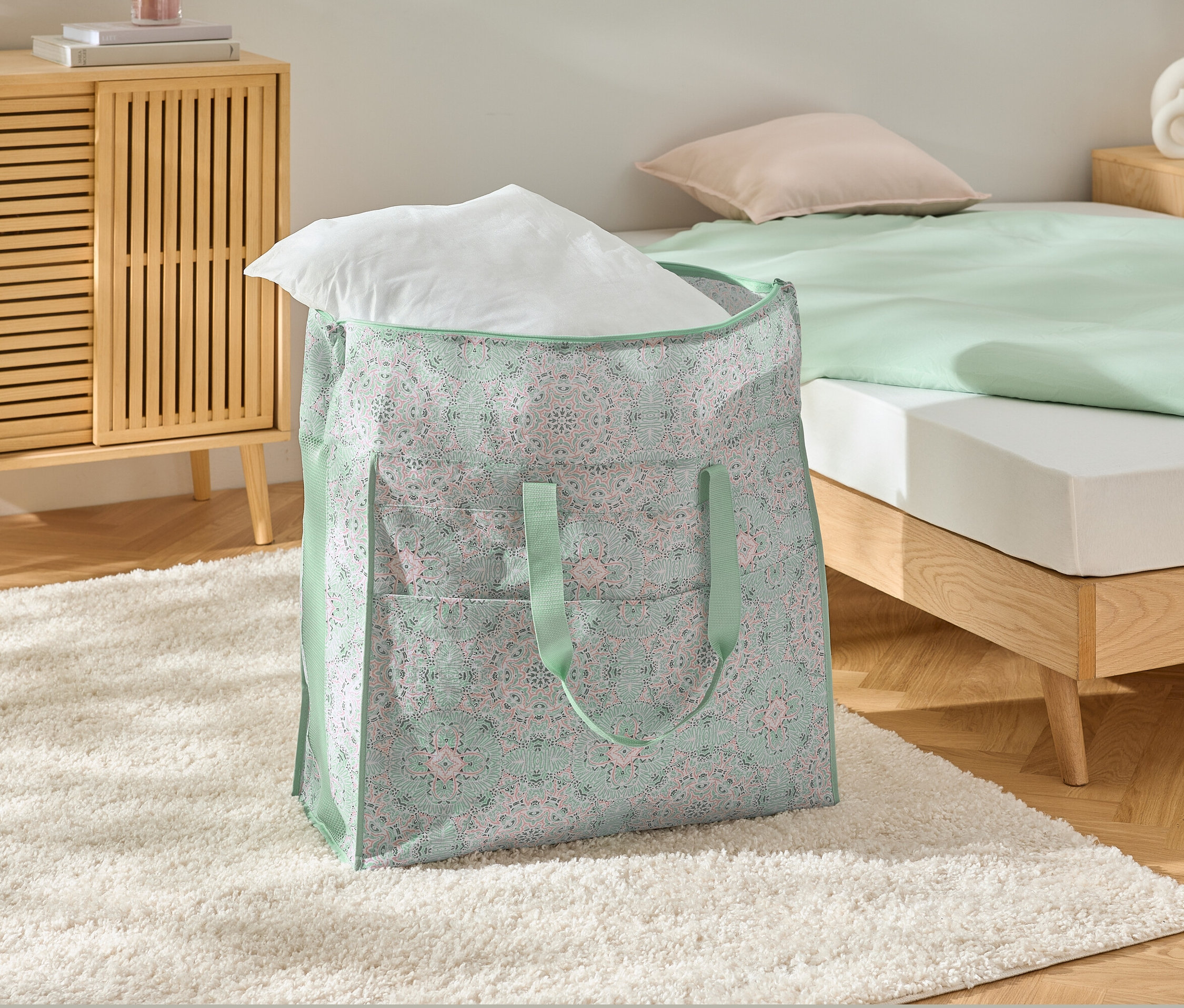 Velká taška na lůžkoviny s bílým polštářem na bílém koberci.