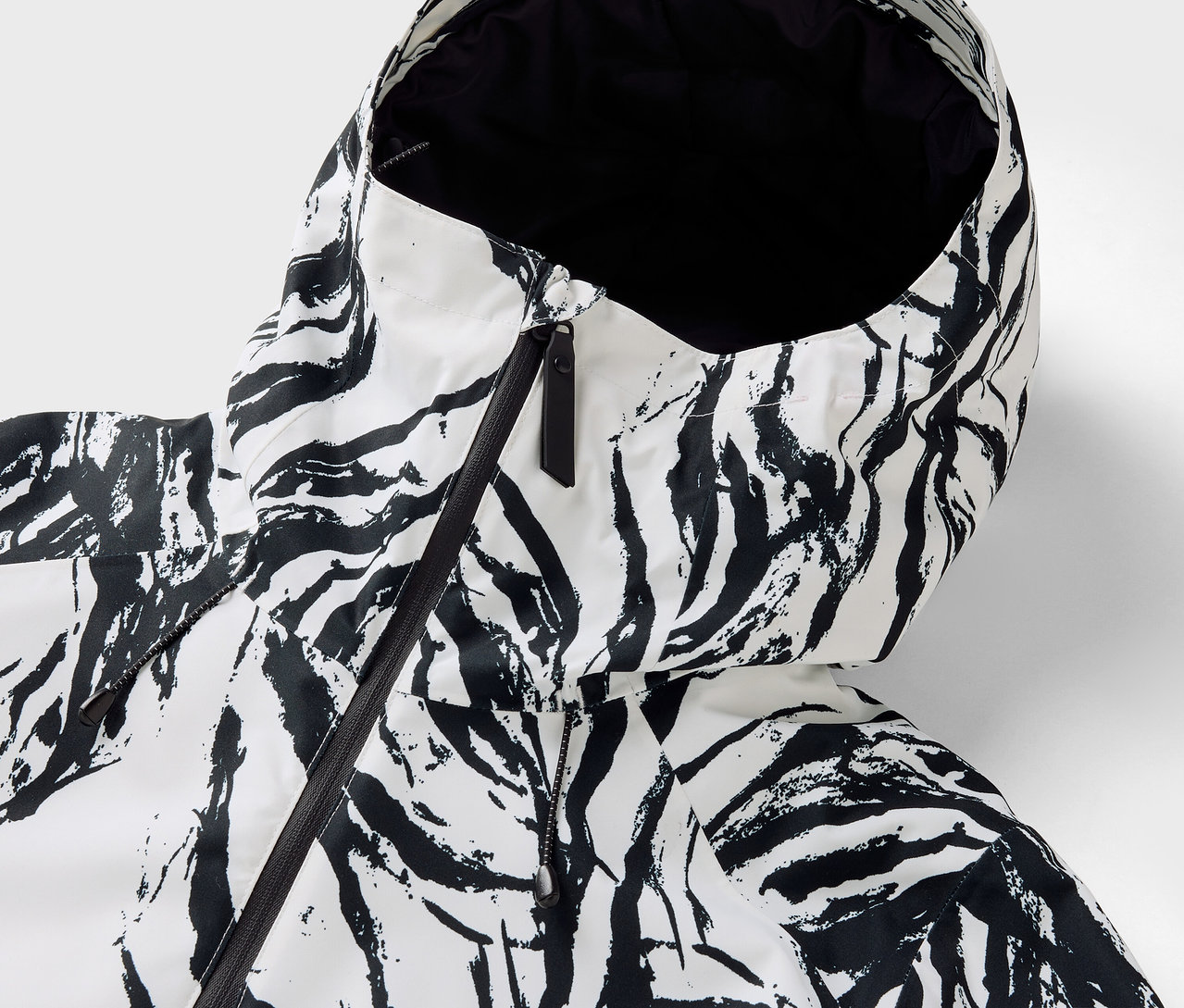 Detail kapuce bundy se vzorem zebra, černý zip.