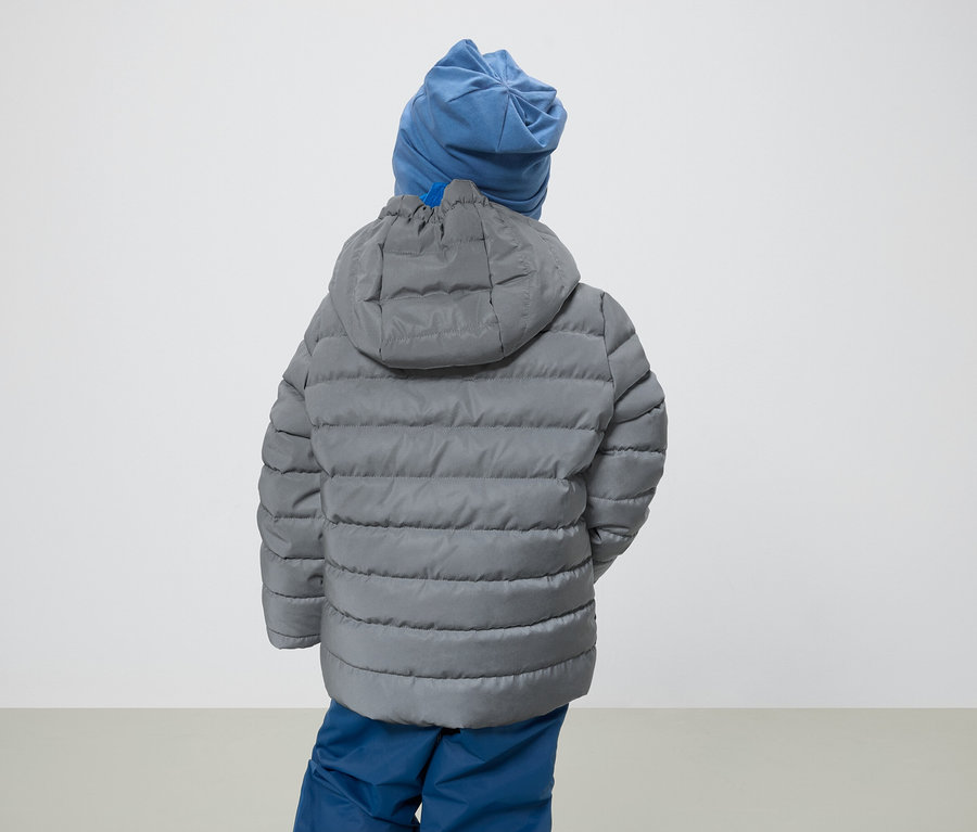 Chlapec zády ke kameře má na sobě šedou bundu s kapucí a modrou čepici.