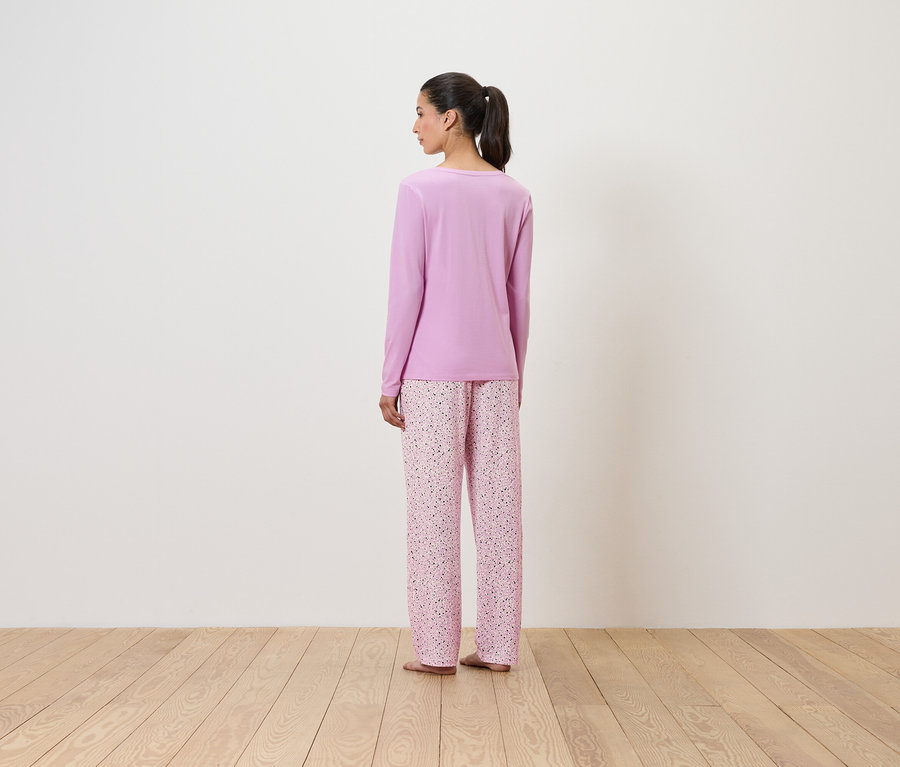 Žena v lila pyžamu s květinovým vzorem, stojící zády k divákovi.