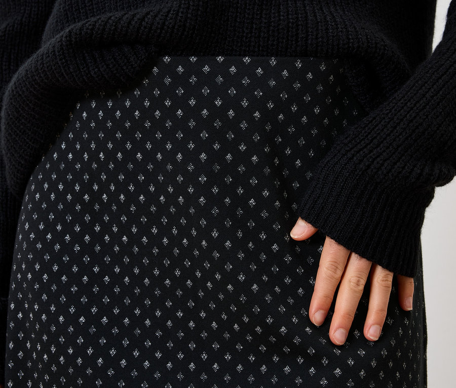 Detail dámské černé sukně s drobným vzorem a černého svetru.