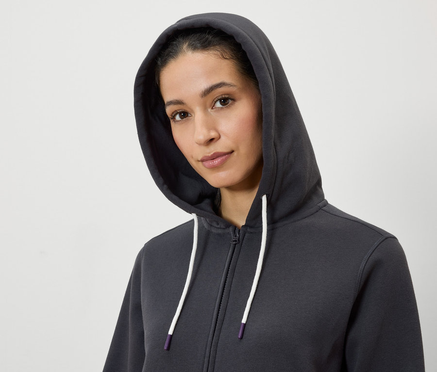 Portrét ženy s kapucí na sobě šedou mikinu na zip s bílými šňůrkami.