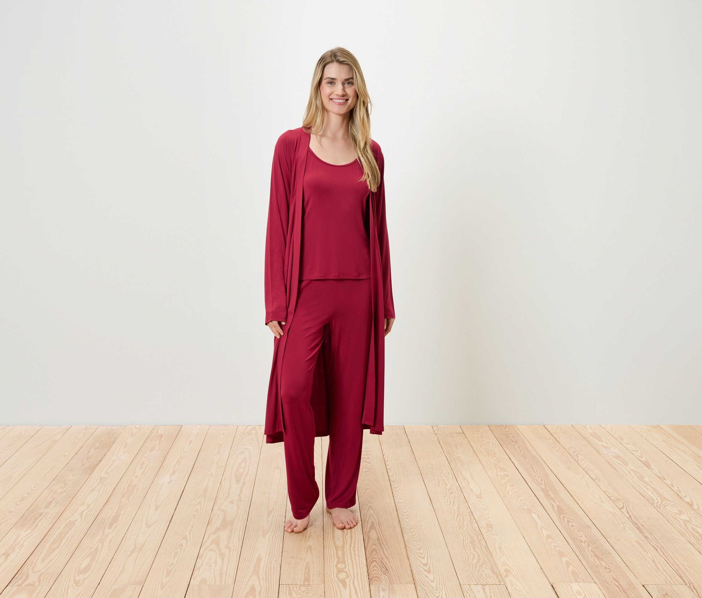 Žena stojí a má na sobě vínové pyžamo, které se skládá z tílka, kalhot a županu.