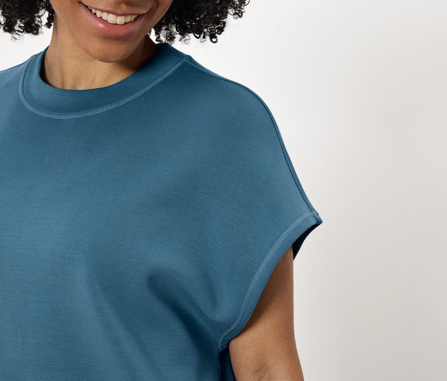 Žena s úsměvem nosí modrozelené tričko.