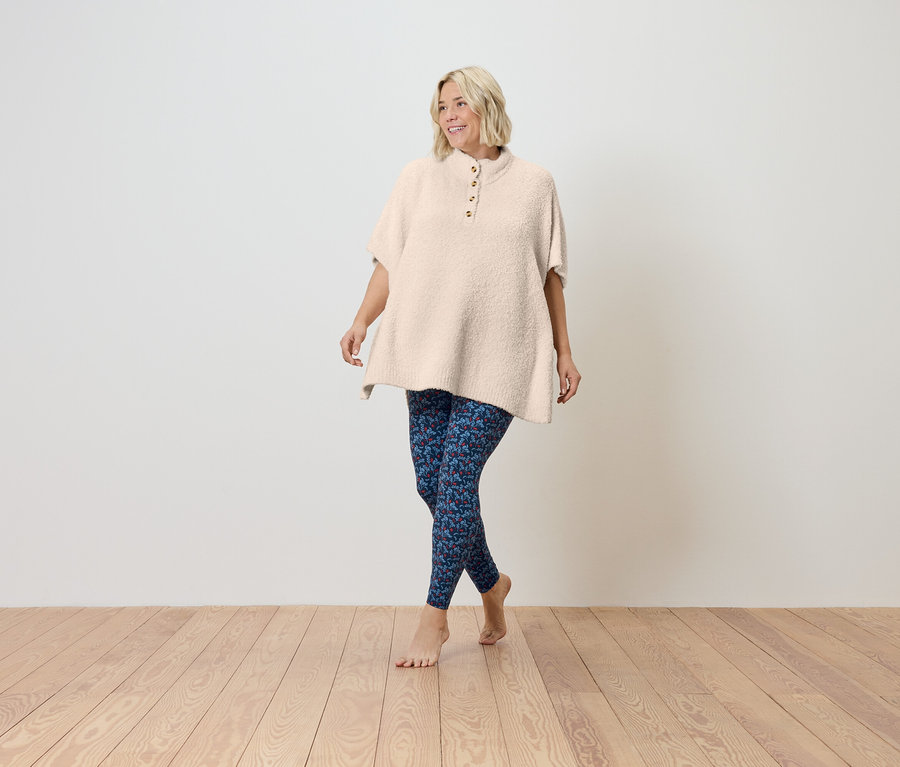 Žena kráčí po dřevěné podlaze v krémové tunice s krátkým rukávem a modrých legínách.