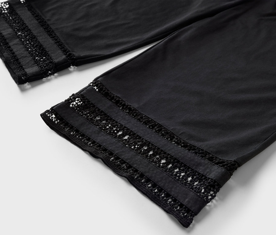 Detail černých culotte kalhot s výšivkou na lemu.