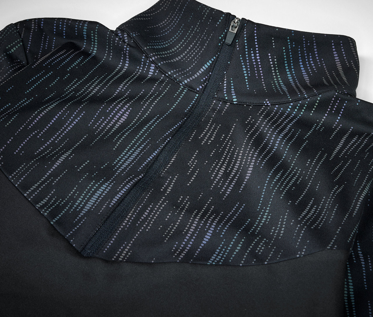 Detail černého sportovního oblečení s ozdobným zipem a vzorem.