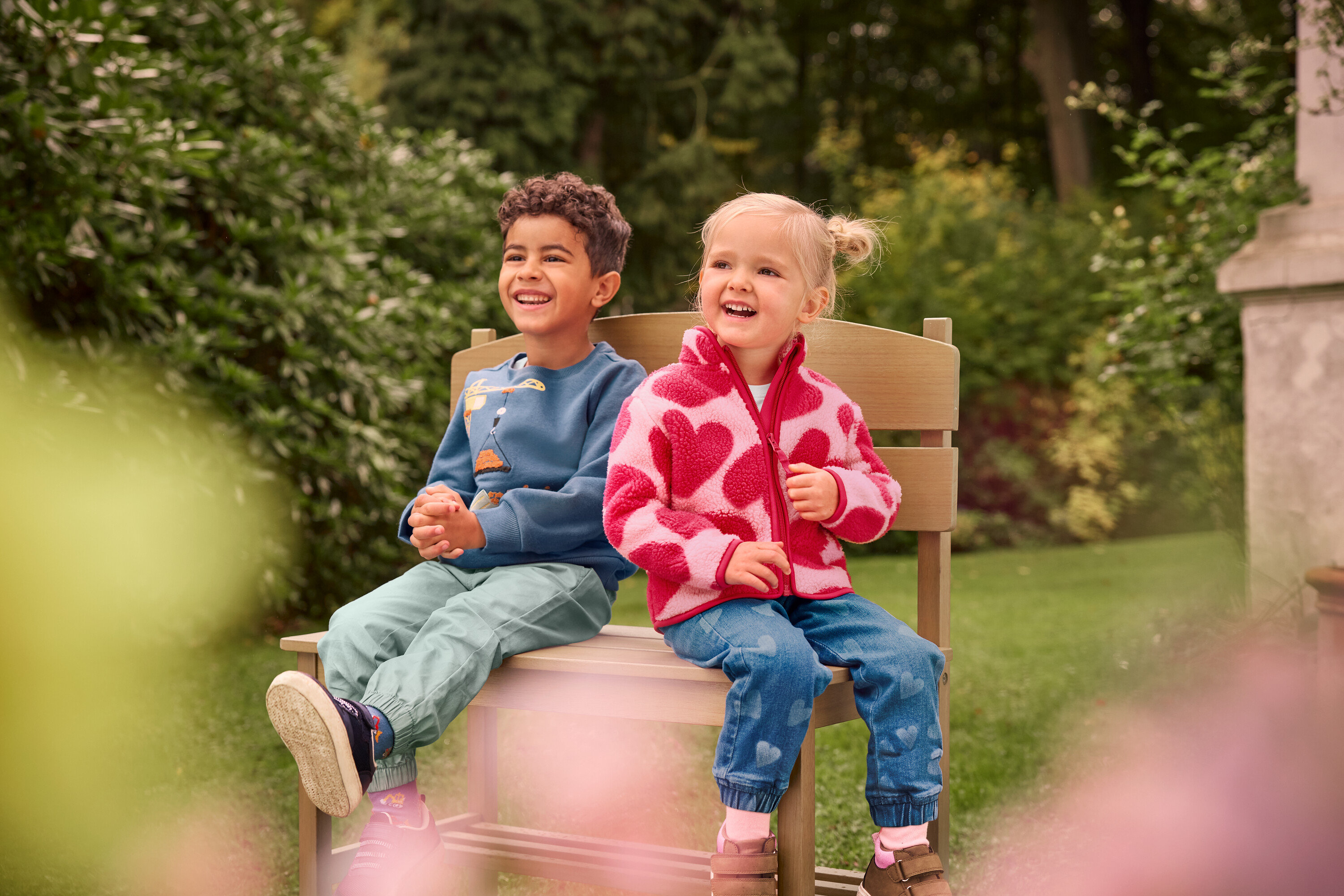 Chlapec a dívka sedí a smějí se na malé zahradní lavičce s přihrádkou.