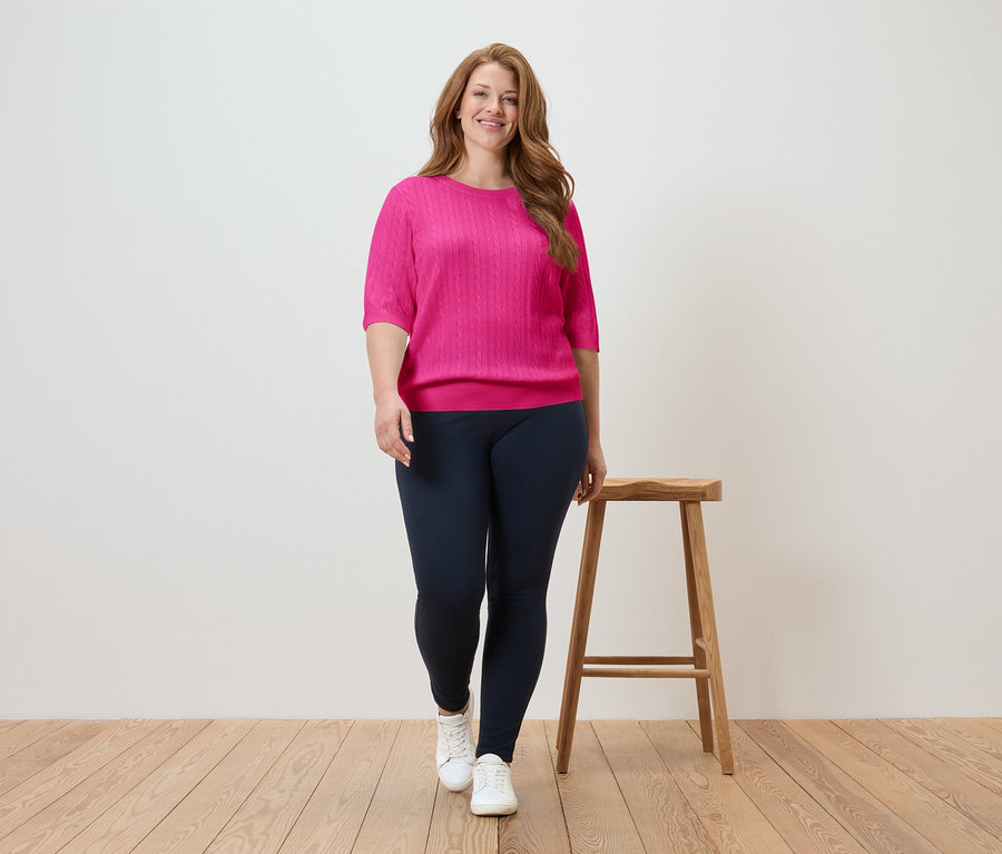 Žena kráčí v růžovém topu a tmavě modrých legínách na dřevěné podlaze