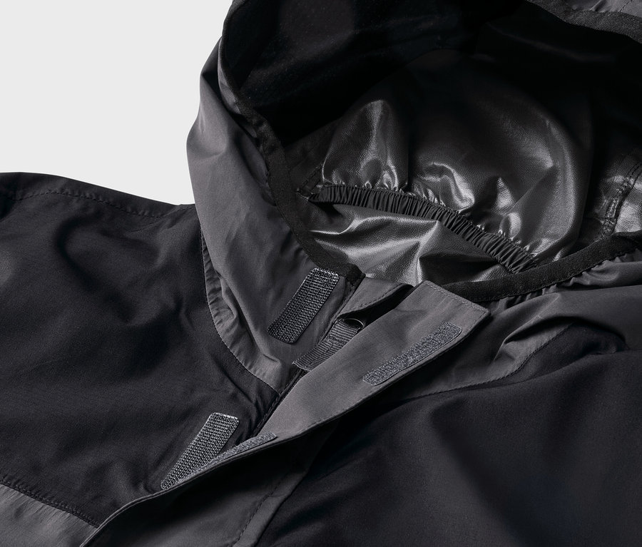 Detailní záběr černé bundy s kapucí, která se zapíná na suchý zip.