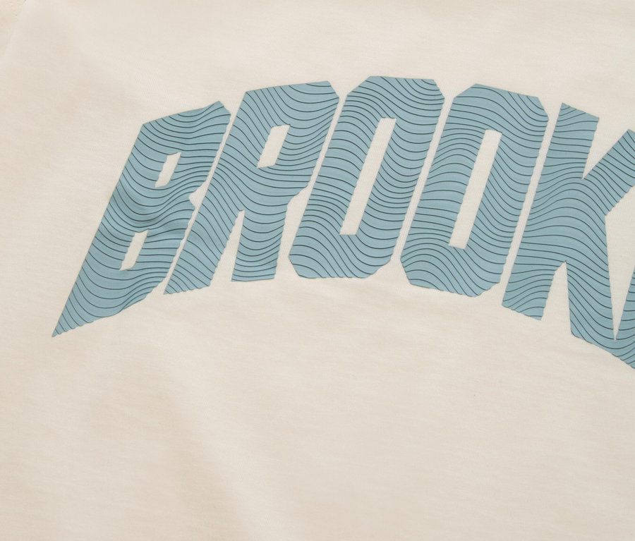 Detailní záběr krémového trička s modrým nápisem „BROOKLYN“.