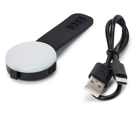 Na bílém pozadí leží černé, kulaté LED světlo s černou rukojetí a USB kabelem.