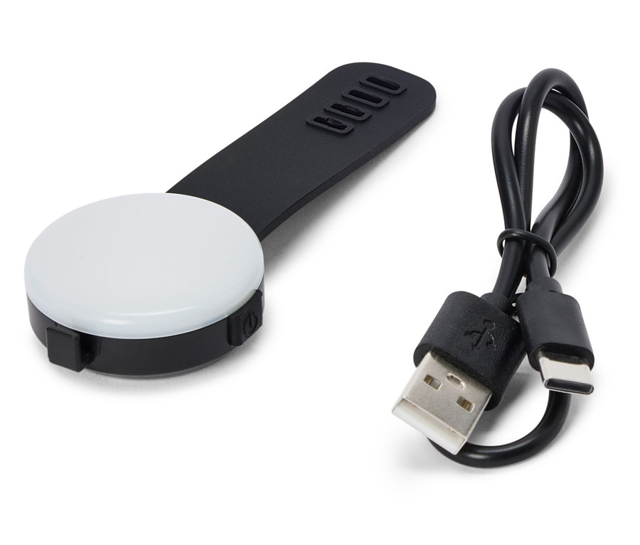 Na bílém pozadí leží černé, kulaté LED světlo s černou rukojetí a USB kabelem.