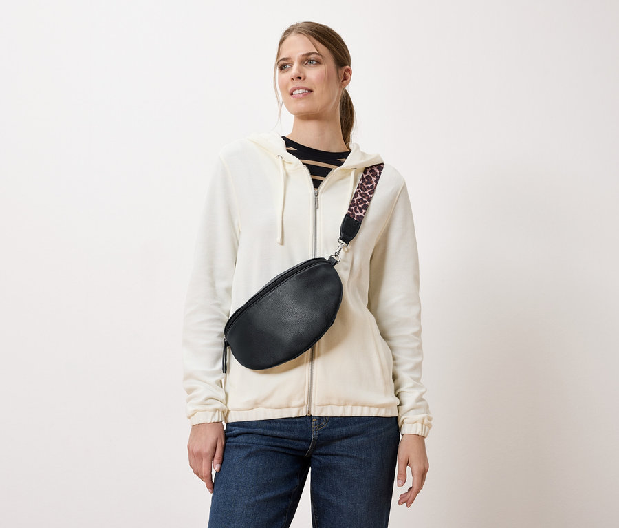 Žena nosí černou ledvinku s popruhem s leopardím vzorem přes krémovou bundu a džíny.