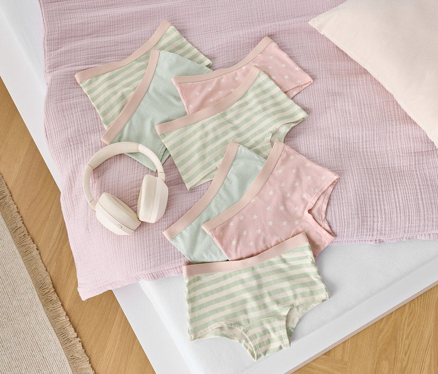 Na posteli leží bavlněné prádlo s proužky a hvězdami vedle bílých sluchátek.