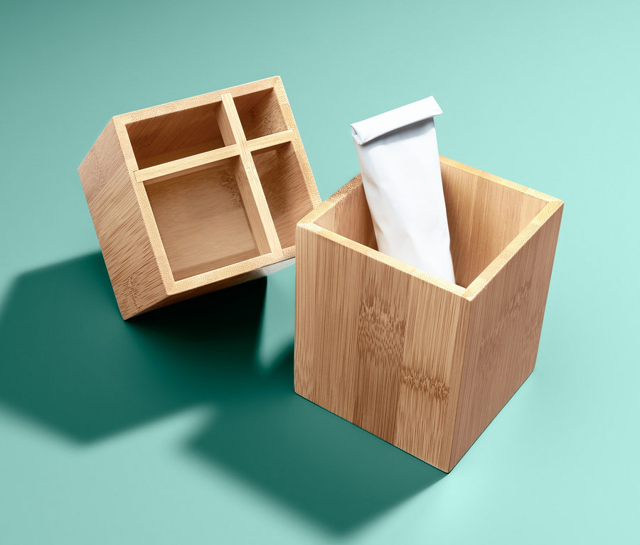 Dva bambusové organizéry na tyrkysovém pozadí, jeden prázdný a druhý s bílou tubou.