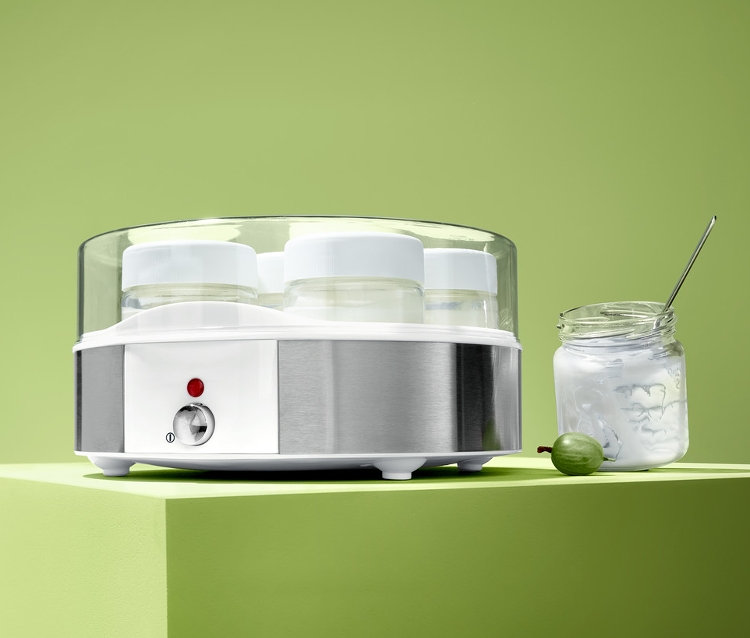 Elektrický jogurtovač se sedmi sklenicemi stojí vedle sklenice jogurtu a zeleného angreštu.