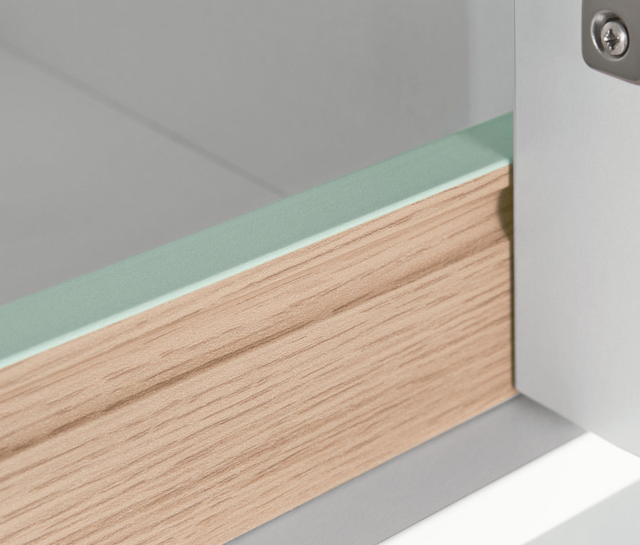 Detail úzké koupelnové skříňky s dřevěnou zásuvkou a zeleným lemem.