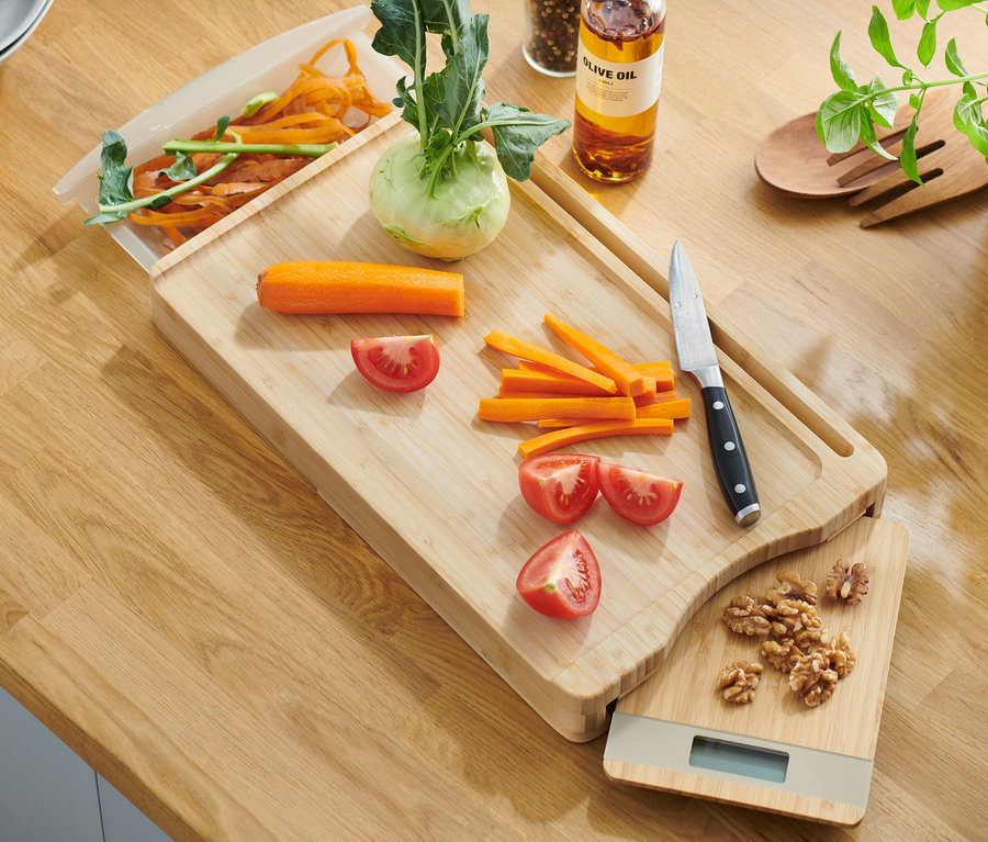 Bambusové krájecí prkénko s vyjímatelnou kuchyňskou váhou, na kterém leží nakrájená zelenina a nůž.