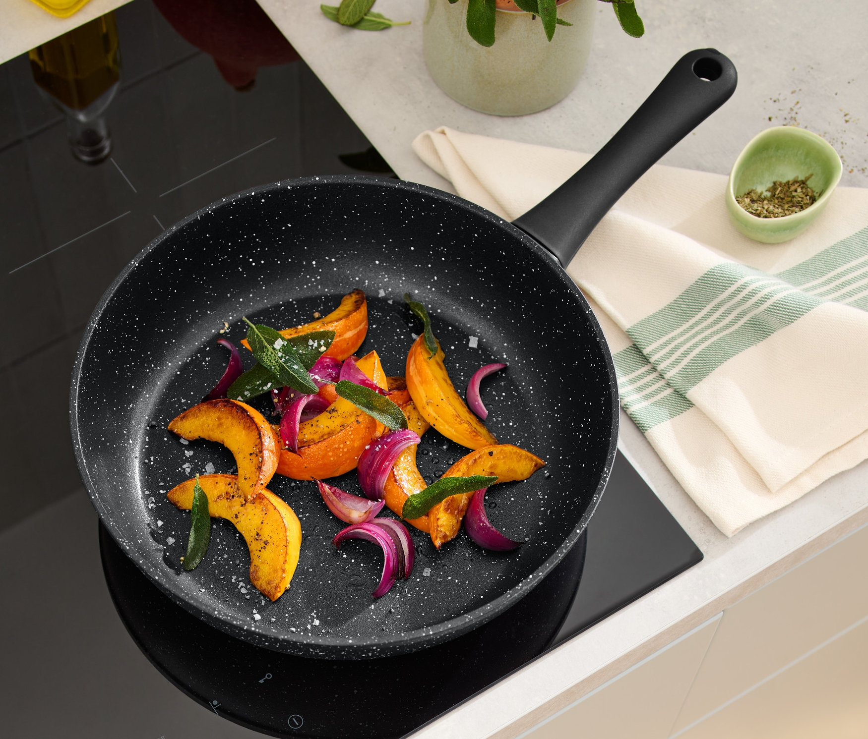 Na indukční desce leží 28cm profi pánev v kamenném vzhledu s pečenou zeleninou.