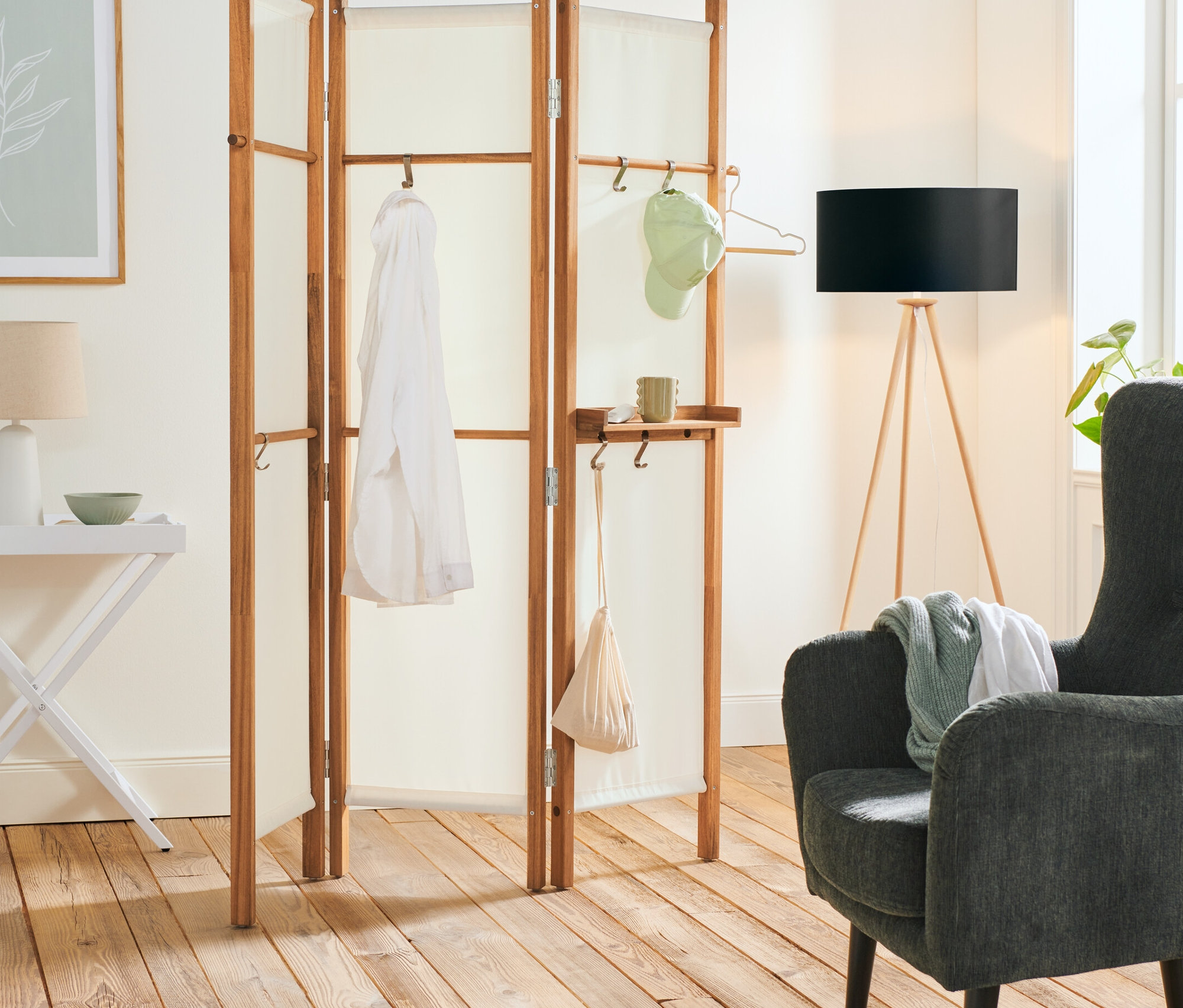 Interiér s dřevěnou stojací lampou »Trojnožka«, skládacím servírovacím stolkem, paravánem s policí a polstrovaným křeslem v antracitové barvě.