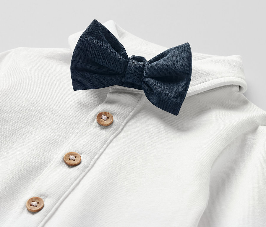 Detail bílého body s motýlkem pro miminka, zapínání na dřevěné knoflíky.