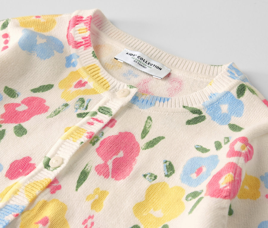 Detail dívčího pleteného svetru s květinovým vzorem.