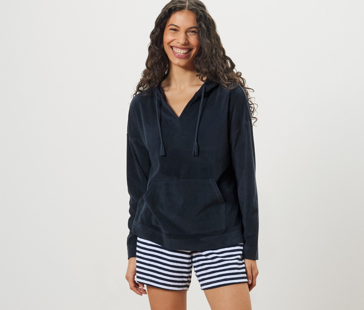 Žena má na sobě froté mikinu s kapucí a pruhované šortky.