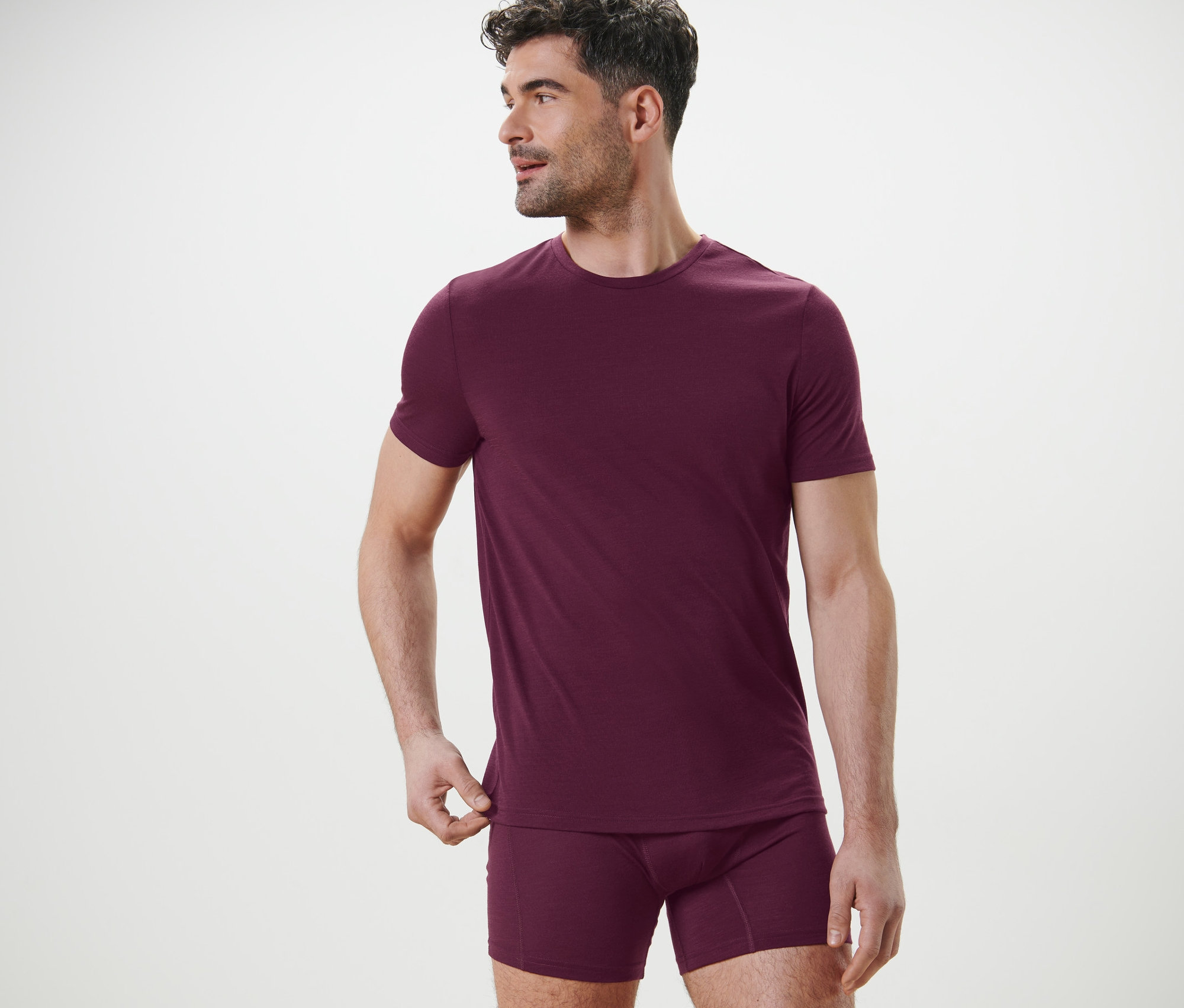 Muž pózuje v bordovém funkčním tričku s vlnou merino a boxerkách.