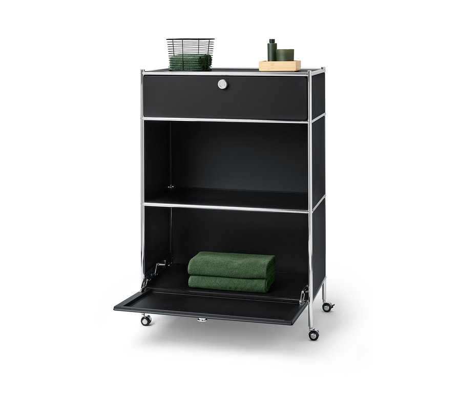 Černá kovová komoda »CN3« s jednou zásuvkou nahoře, na které leží košík s ručníky, a jedněmi výklopnými dvířky dole, na kterých leží dva ručníky.