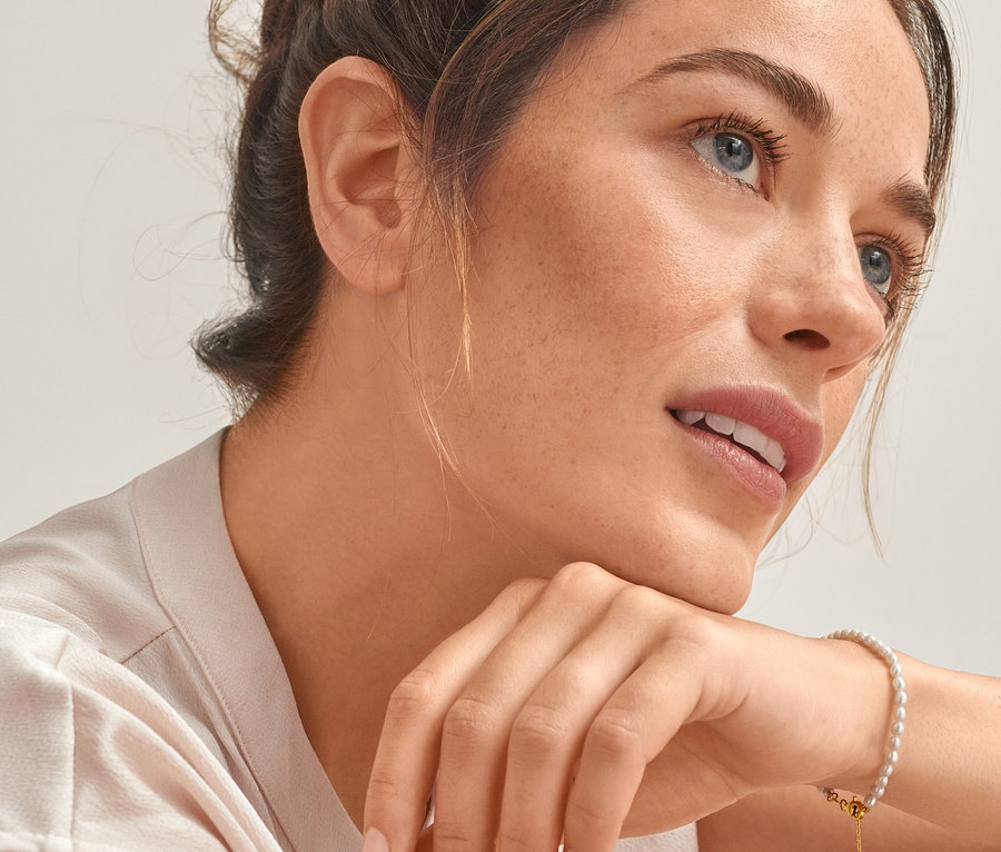 Portrét ženy s hnědými vlasy v drdolu, která se opírá bradou o ruku, na které má náramek ze zlaceného stříbra 925/1000 se sladkovodními perlami.