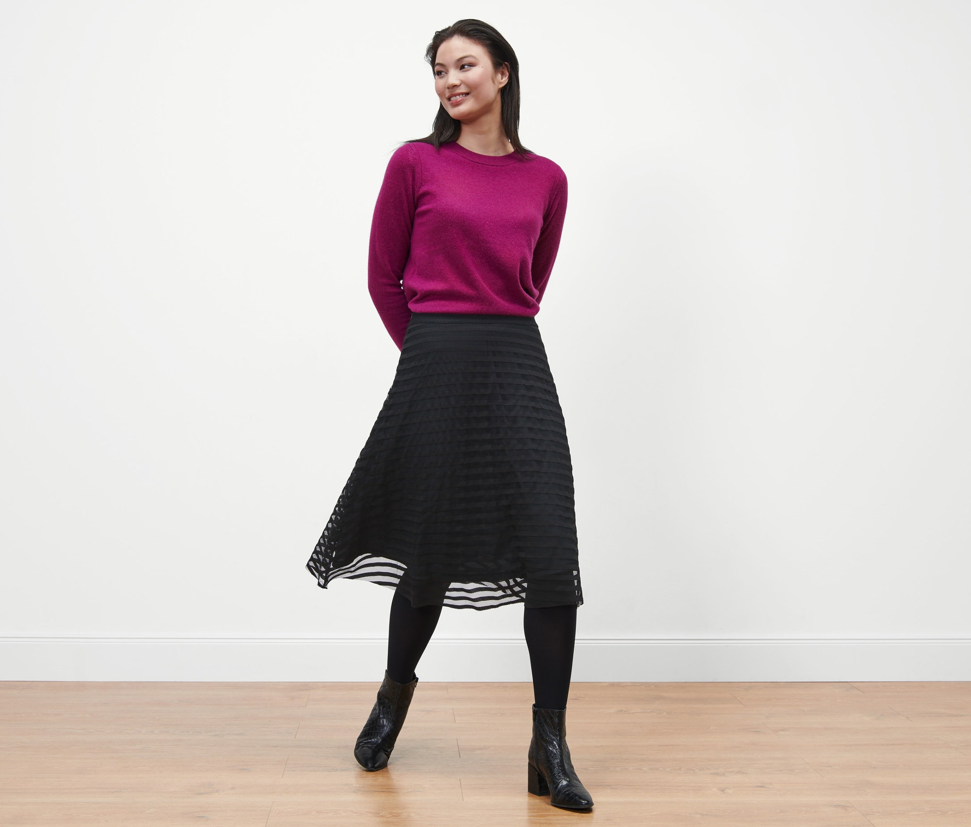Žena pózuje v purpurovém svetru a černé síťované sukni.